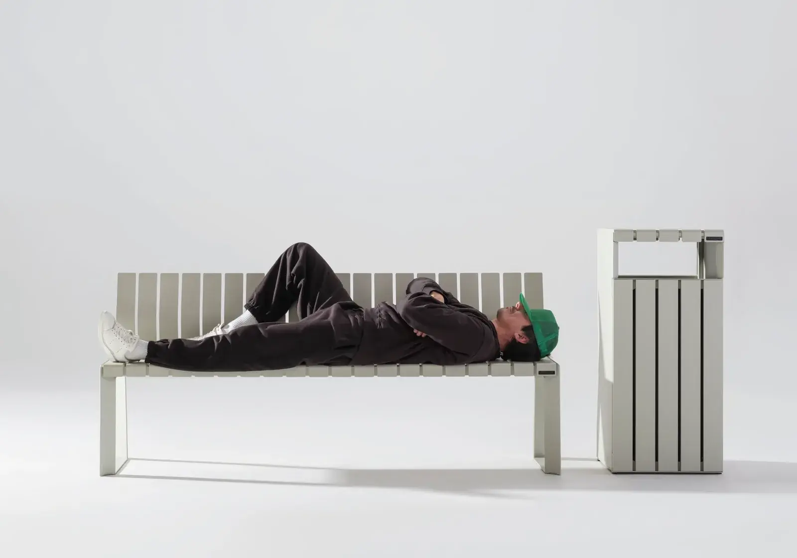 Man lying on a white Liberty.080 bench beside its litter bin