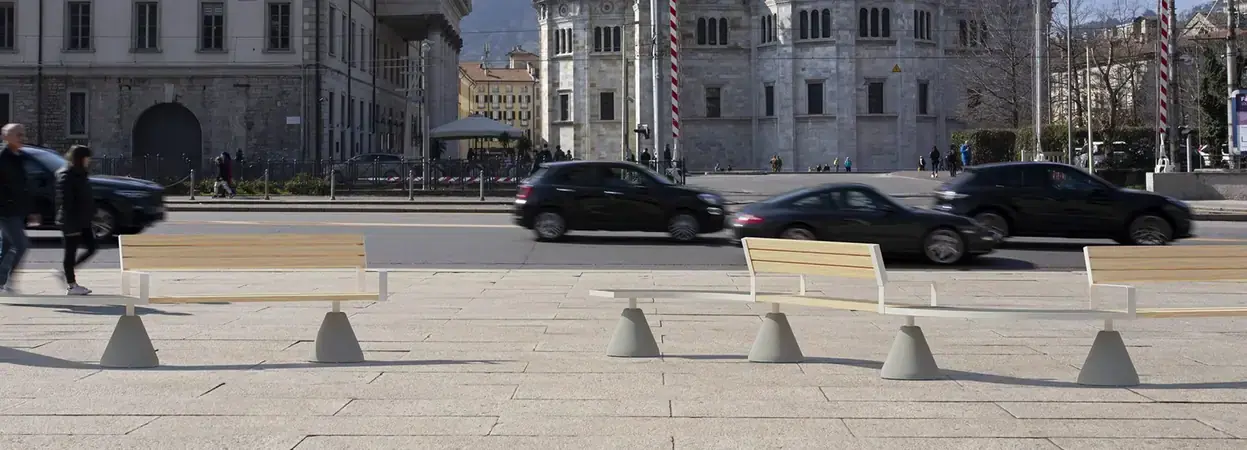 Sempreverde benches on concrete cone bases along a street in Como, the cathedral and passing traffic behind