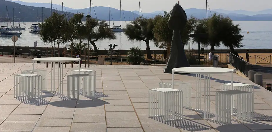 Zeroquindici.015 tall round tables and stools on a harbourside courtyard, moored boats and hills behind